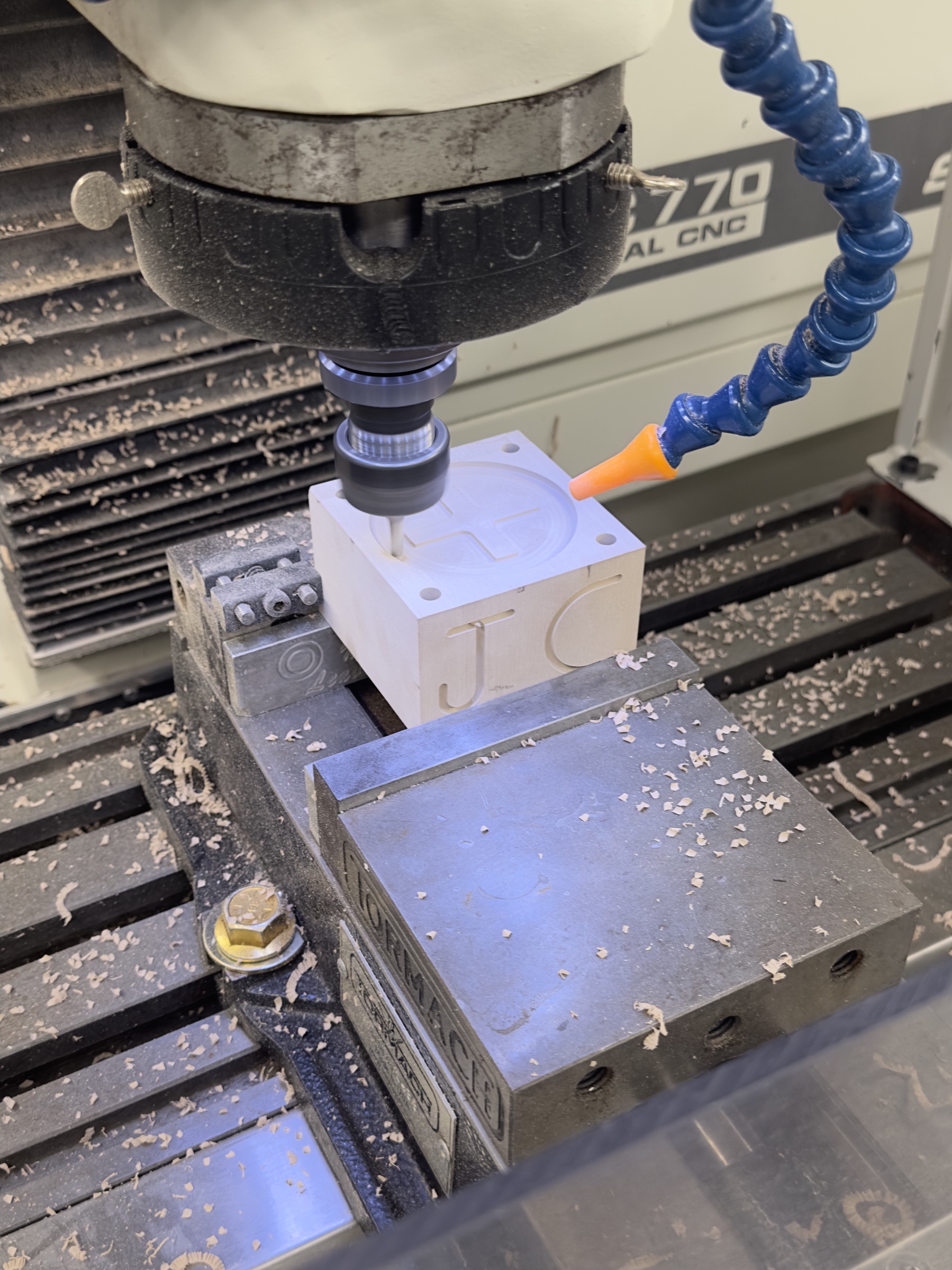 CNC mill cutting a cross-shaped cavity into an aluminium mould block, JC carved into its side