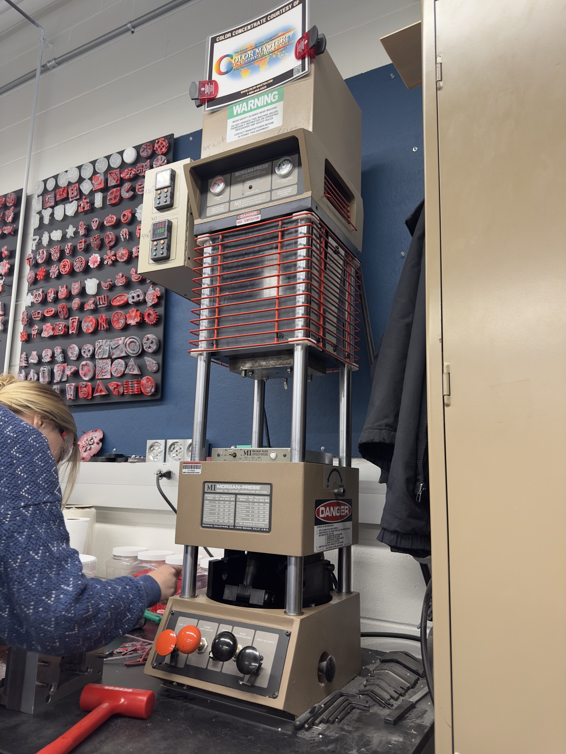 Morgan-Press benchtop injection moulding machine, with a board of moulded parts on the wall behind it